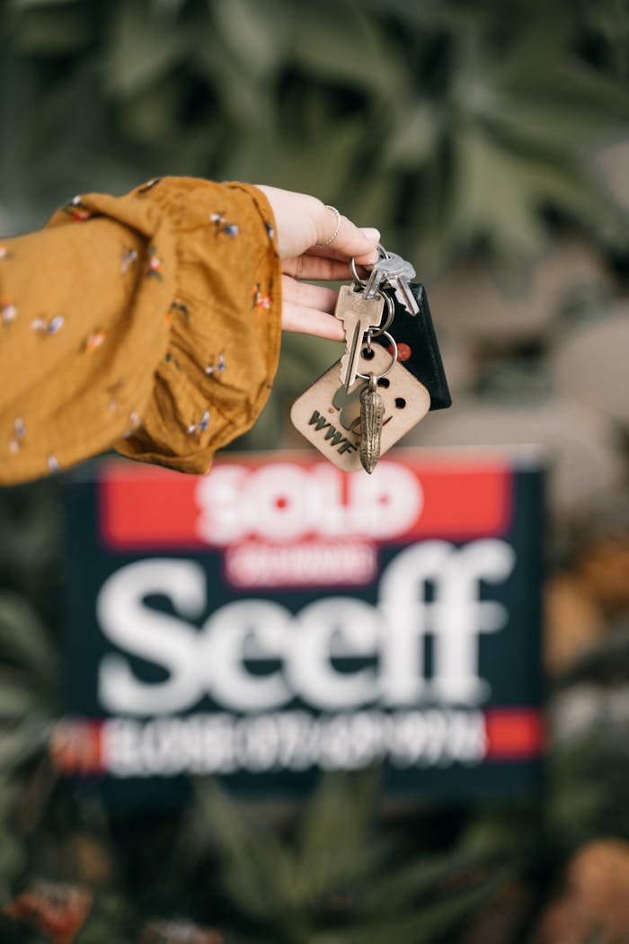 about-us A hand holds keys in front of a blurred sold real estate sign, symbolizing completed sale.